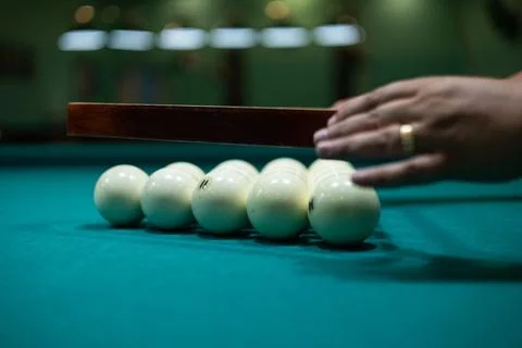 Having collected the billiard balls into a triangle, the man aligns them on the Stock Photos