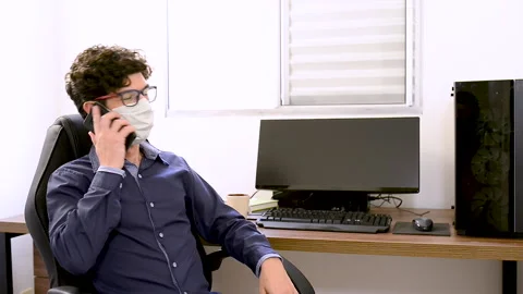Having a conversation over smartphone wearing a mask at Office. Video stock 135141604