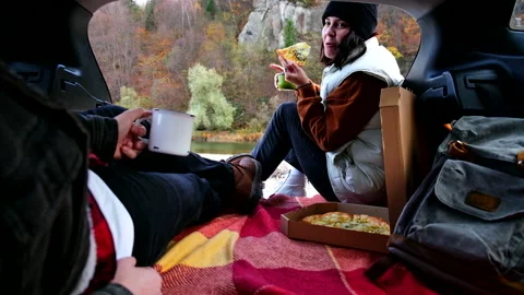 Having picnic in car trunk and eating pizza while drinking tea at autumn river Stock Footage 237070082