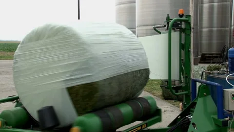 The hay wrapping machine covers the bale of hay with a plastic wrap. Video stock 134580734