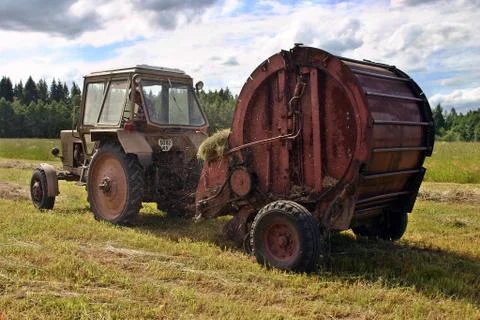 Haymaking time, round baling hay and farming tractor in farmland. Stock Photos