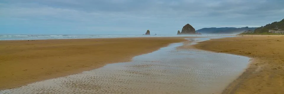 Haystack Rock Reflects In The Low Tide Of Canon Beach On Cloudy Morning. Stock Photos