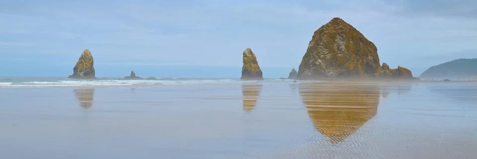 Haystack Rock Reflects In The Low Tide Of Canon Beach On Cloudy Morning. Stock Photos