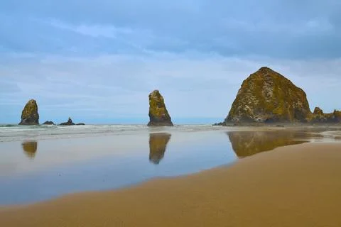 Haystack Rock Reflects In The Low Tide Of Canon Beach On Cloudy Morning. Stock Photos