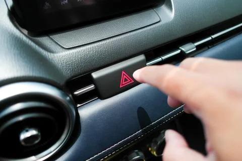 The hazard or emergency light button is pressed by the driver hand Foto stock