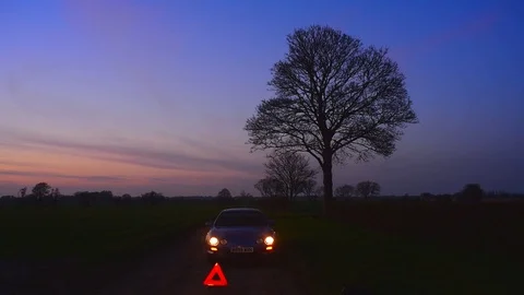 Hazard warning triangle by broken down car on country road at twilight uk Stock Footage 106183749