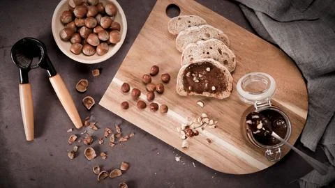 Hazelnut spread on bread slices with whole nuts and a nutcracker Stock Photos