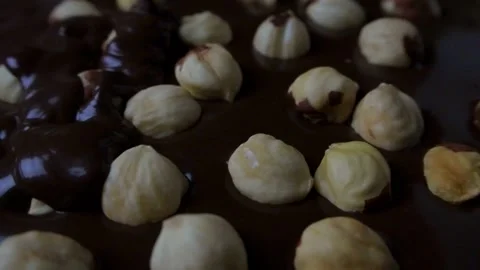 Hazelnuts are in chocolate and chocolate is pouring on top Stock Footage 147254400
