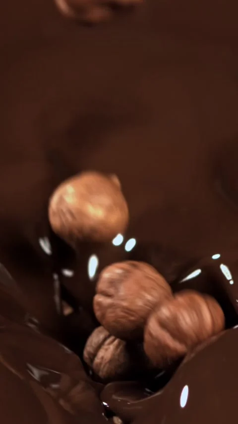 The hazelnuts fall into the liquid chocolate. Filmed on a high-speed camera at Stock Footage 335377557
