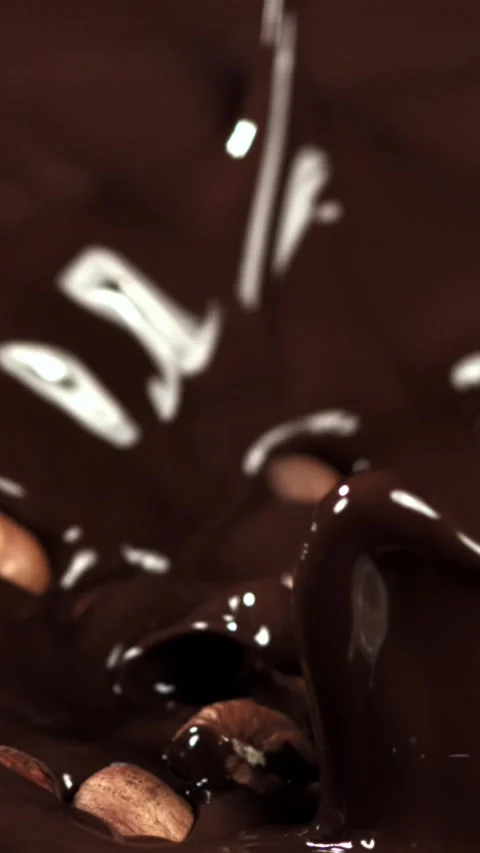 The hazelnuts fall into the liquid chocolate. Filmed on a high-speed camera at Stock Footage 335380296