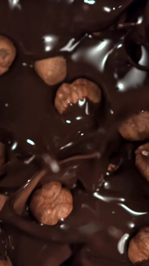 The hazelnuts fall into the liquid chocolate. Filmed on a high-speed camera at Stock Footage 335380631