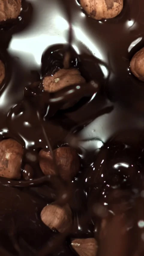 The hazelnuts fall into the liquid chocolate. Filmed on a high-speed camera at Stock Footage 335383970