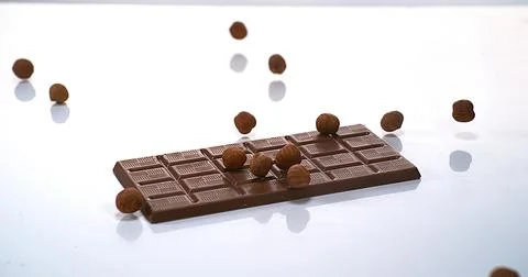 Hazelnuts falling on Milk Chocolate tablet Stock Photos