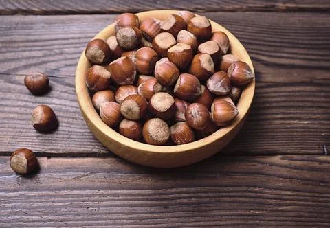 Hazelnuts in a shell in a wooden bowl, empty space on the left Stock Photos