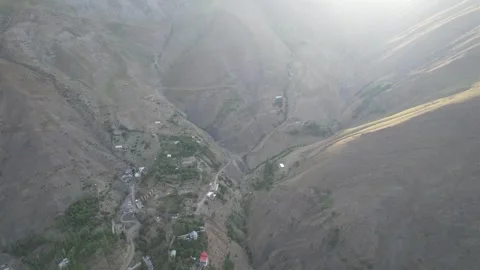 Hazy aerial down a Shem mountain valley shows a thin green line and distant Stock Footage 343804715