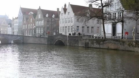 Hazy sunshine view down a canal Bruges, Belgium. Walkers, Cyclists, cars driving Stock Footage 45258988