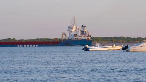 HD Cargo ship in background passing behind fishing boats on beach Stock Footage 75423913