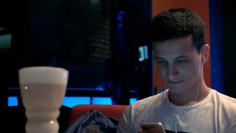 HD Man sits in a cafe looking into his phone with headphones. There is latte on Vidéo 99991381