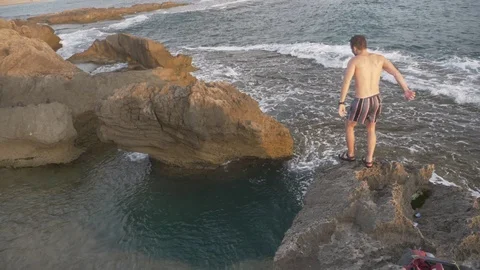 HD slow motion young man jumping from high rocky ledge Into the ocean. Stock Footage 116060472