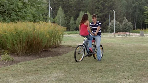 HD A yound couple is sitting on one bycile looking at each other and cahtting 库存影片 94443653