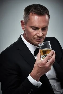 He enjoys a well-aged scotch. Portrait of a tuxedo-clad mature man holding a Stock Photos