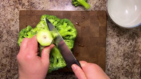 A head of broccoli is separated into florets using a knife against wooden board. Video stock 321153296