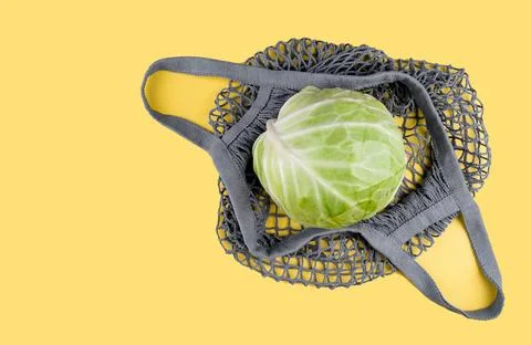 A head of cabbage lies in ecological string bag on a yellow background Stock Photos