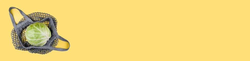 A head of cabbage lies in an ecological string bag on a yellow background. Stock Photos