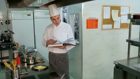 Head chef looking for recipe in a cookbook while checking upon his trainee Vídeos de archivo 72322255