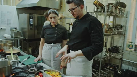 Head Chef Telling about Dish to Female Apprentice in Restaurant Kitchen Stock Footage 270140850