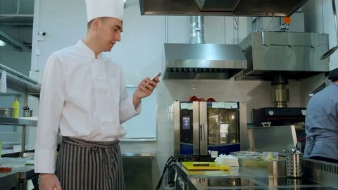 Head cook standing in the kitchen and using his cell phone Video stock 72324205