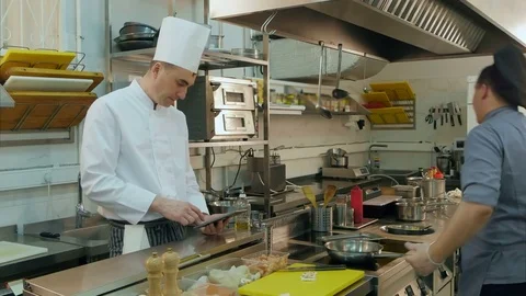 Head cook using tablet while young assistant preparing pan Stock Footage 72322349