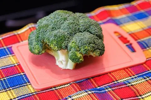 A head of green broccoli on a pink plastic cutting board, and colorful towel Stock Photos