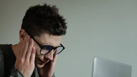 Headache due to overwork. Close-up of young man in glasses holding his head Stock Footage 308073431