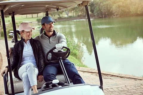 Heading down the fairway. a smiling young couple riding in a cart on a golf Fotos Stock