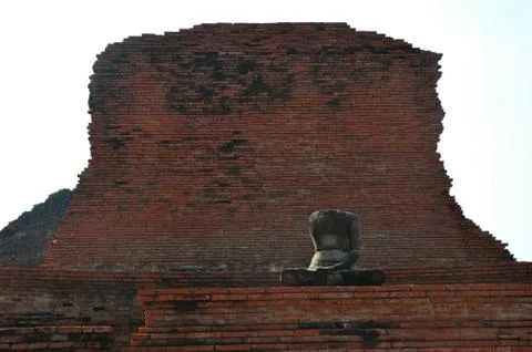 A headless Buddha dwarfed by a stone wall Stock Photos
