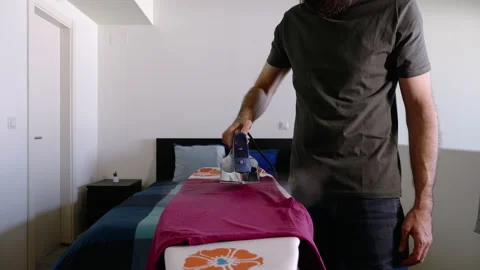 Headless shot of bearded man ironing a T-shirt on an ironing board at home Stock Footage 131229514