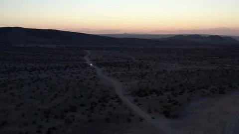 Headlights of car driving on desert dirt road at sunset, wide aerial Stock Footage 195199630