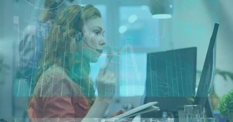 Headset-wearing agent taking notes in notebook at office desk, with monitors and Stock Photos
