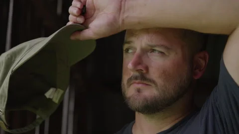 Headshot of 30 Something Farmer with Beard Wiping Sweat Off Forehead in barn Stock Footage 217769049