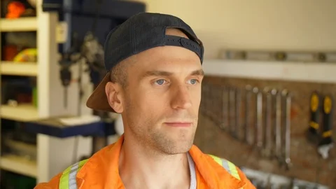 Headshot of Man Wearing Backwards Hat and Safety Coveralls in Mechanics Shop Stock Footage 90797035