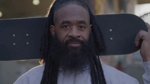 Headshot Portrait of Diverse Man with Dreadlocks and Beard Holding Skateboard in Stock Footage 270397877