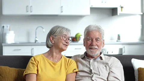Headshot portrait of smiling elderly 60s husband and wife sit relax on couch hug Stock Footage 237939254