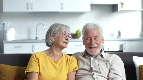 Headshot portrait of smiling elderly 60s husband and wife sit relax on couch hug Stock Footage 237939255