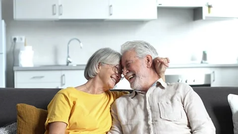 Headshot portrait of smiling elderly 60s husband and wife sit relax on couch hug Stock Footage 237939364