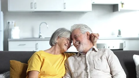 Headshot portrait of smiling elderly 60s husband and wife sit relax on couch hug Stock Footage 237939445