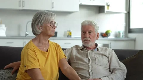 Headshot portrait of smiling elderly 60s husband and wife sit relax on couch hug Stock Footage 237939724