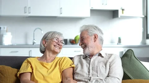 Headshot portrait of smiling elderly 60s husband and wife sit relax on couch hug Stock Footage 237939959