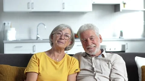 Headshot portrait of smiling elderly 60s husband and wife sit relax on couch hug Stock Footage 237940155