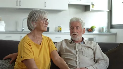 Headshot portrait of smiling elderly 60s husband and wife sit relax on couch hug Stock Footage 237940184